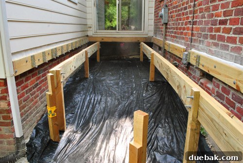 Unrolling and securing weed block fabric across the ground under the deck structure.