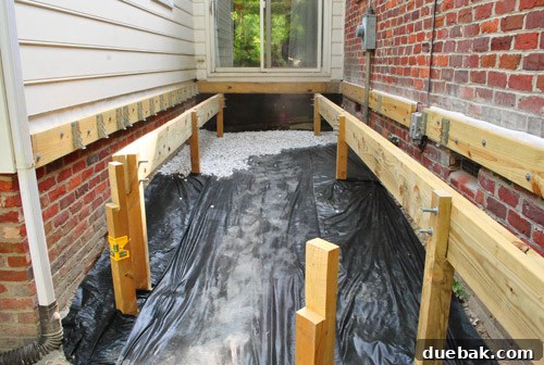 Spreading gravel over the weed block, covering the ground beneath the deck.