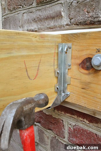 Installing a metal joist hanger onto the brick side of the house ledger board.