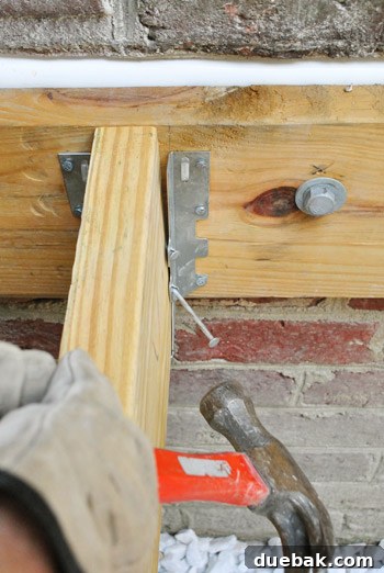 Close-up of angled nails being driven into a joist hanger for side stability.