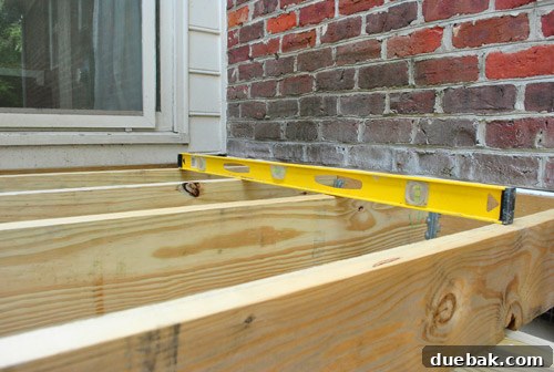 Using a level to check the alignment and slope of a newly installed deck joist.