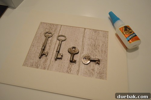 Antique keys glued onto wood-grain paper, drying on a protected surface.