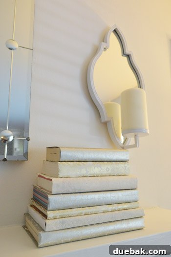 A beautifully styled fireplace mantel with candle sconces, a leaf wreath, and books covered in decorative paper.