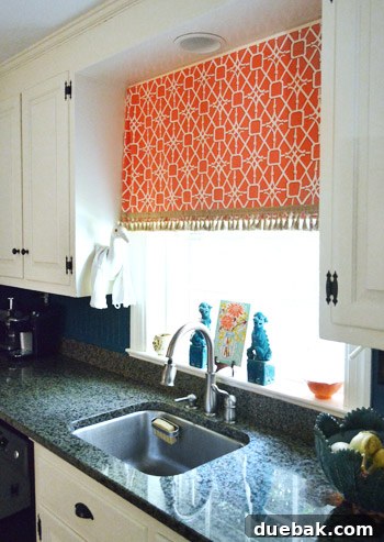 Kitchen details: a vibrant fabric curtain with fringe, a unique crane holding a dishtowel, and decorative aqua foo dogs