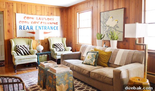 Cozy family room with original wood paneling, layered textiles, vintage laundry sign, and thrifted wing chairs