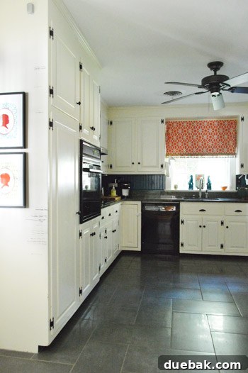 Kitchen with dark herringbone tile floors, DIY beadboard backsplash, creamy white cabinets, and dark hardware