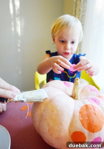 Three Playful Pumpkin Crafts for Little Ones 5 Clara placing tissue paper dots on a pumpkin coated with Mod Podge
