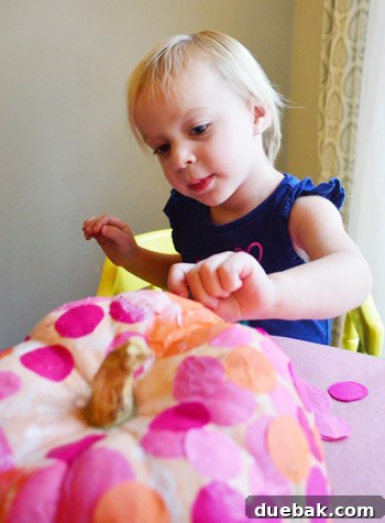 Three Playful Pumpkin Crafts for Little Ones 8 Clara deeply focused on applying tissue paper to the pumpkin