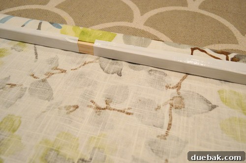 Fabric being rolled around the wood header and secured with white duct tape on the back