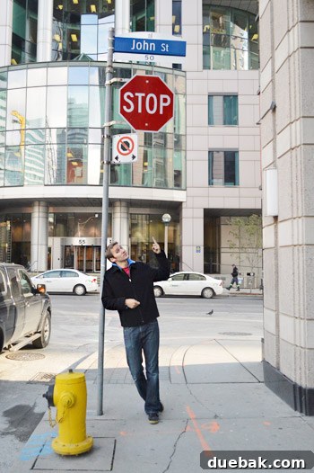 New York, Richmond, Chicago, Toronto: City Tapestry 25 John posing under a sign with his name
