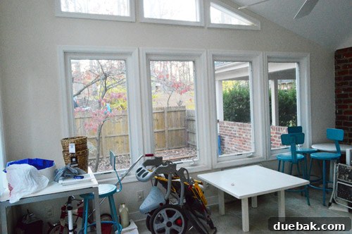 The sunroom's wall overlooking the side patio, with large windows emphasizing the connection to the outdoor living space, still in its original condition.