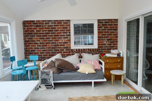 A close-up of the sunroom's brick wall with a window looking into the kitchen, highlighting the unique architectural features and the room's current state.
