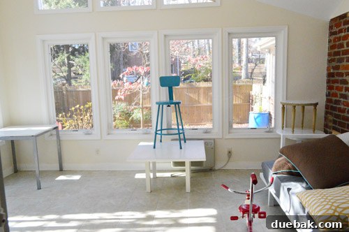 The sunroom partially decluttered, showing progress in removing excess items and revealing more of the floor space, preparing for renovation.