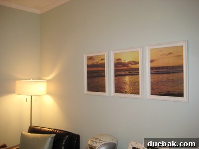 Three framed segments of a Santa Monica sunset photograph above a bed