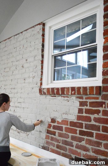 Painter applying gray paint to the brick wall in the sunroom, tackling numerous cracks with a brush.