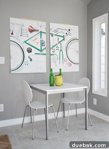 Two bicycle art prints temporarily affixed with masking tape above a table and chairs in the sunroom.