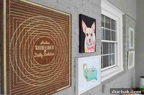 A closer view of the left side art arrangement, featuring a large doily stretcher, a watercolor print, and a pet portrait.