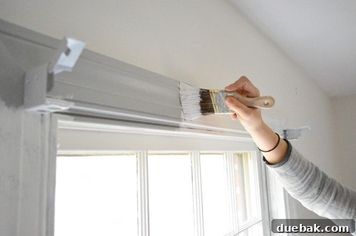 Window trim being painted glossy white, covering previous gray paint