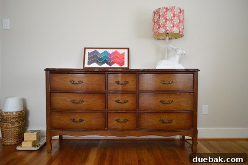 A newly acquired secondhand wooden dresser placed against a white wall in Clara's evolving big girl room, showing its initial placement.