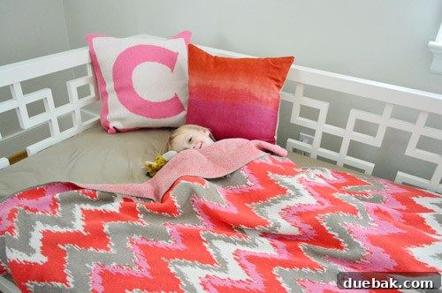 A cute child, Clara, playfully pretending to sleep on the cozy daybed amidst the pillows and blankets in her big girl room.