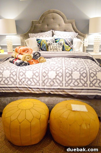 Luxurious bedroom setting with a platinum tufted velvet headboard, complemented by vibrant yellow poufs and colorful pillows.