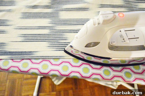 DIY No Sew Ikat Curtains for Playful Kids Spaces 8 Hands carefully ironing hem tape onto the edge of a fabric panel