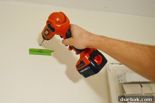DIY No Sew Ikat Curtains for Playful Kids Spaces 9 A close-up of a hand drilling into a wall, with painter's tape folded below to catch dust