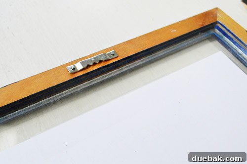 Close-up of a sawtooth hanger being nailed into a wooden frame