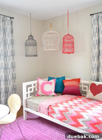 Three decorative birdcages, one white, one red, and one dark pewter, hanging above a daybed in a child's room.