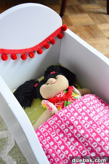 Finished doll cradle with red pom-pom trim and pink blanket