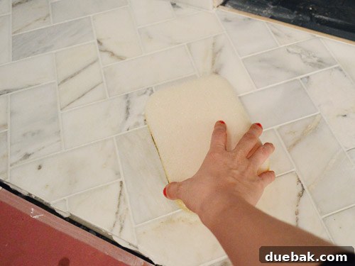 Your Guide to a Stunning Marble Herringbone Fireplace 21 Wiping excess grout from marble tiles