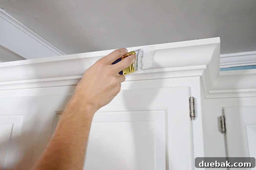 Transform Your Cabinets with Elegant Crown Molding 11 Painting crown molding on a kitchen cabinet with a short handled paint brush
