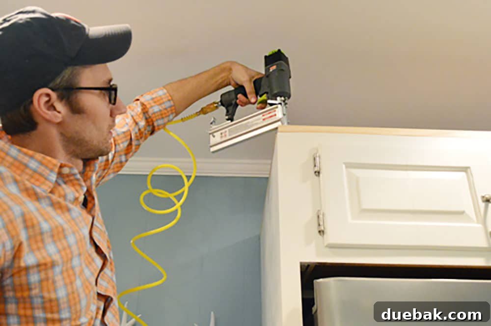 Transform Your Cabinets with Elegant Crown Molding 6 John using nail gun to attached scrap wood to top of cabinet
