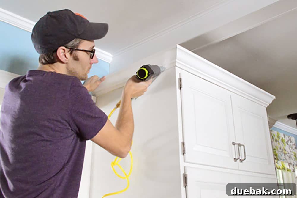 Transform Your Cabinets with Elegant Crown Molding 8 John using nail gun to attach crown molding to the top of the cabinets