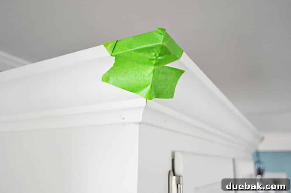 Transform Your Cabinets with Elegant Crown Molding 9 Green painters tape on the corner of kitchen crown molding while glue dries