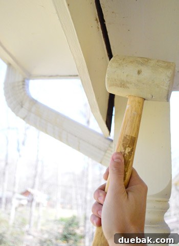 Refreshing Your Porch: Taking Down Scalloped Trim and Repairing Columns 5 The author using a rubber mallet to gently loosen the stubborn scalloped trim from the porch structure.