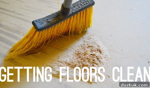 The process of thoroughly cleaning a subfloor before hardwood installation, showing a vacuum cleaner and sweepers.