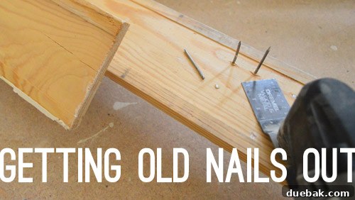 A Dremel tool with a metal cutting bit being used to trim old nails flush with the back of a removed baseboard.