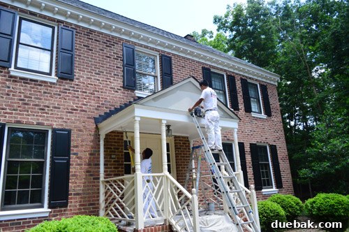 House painter working on high ladder, applying paint to exterior trim