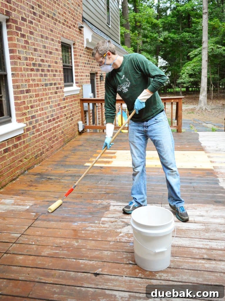 A person applying deck stripper to a wood deck using a paint roller with an extension pole