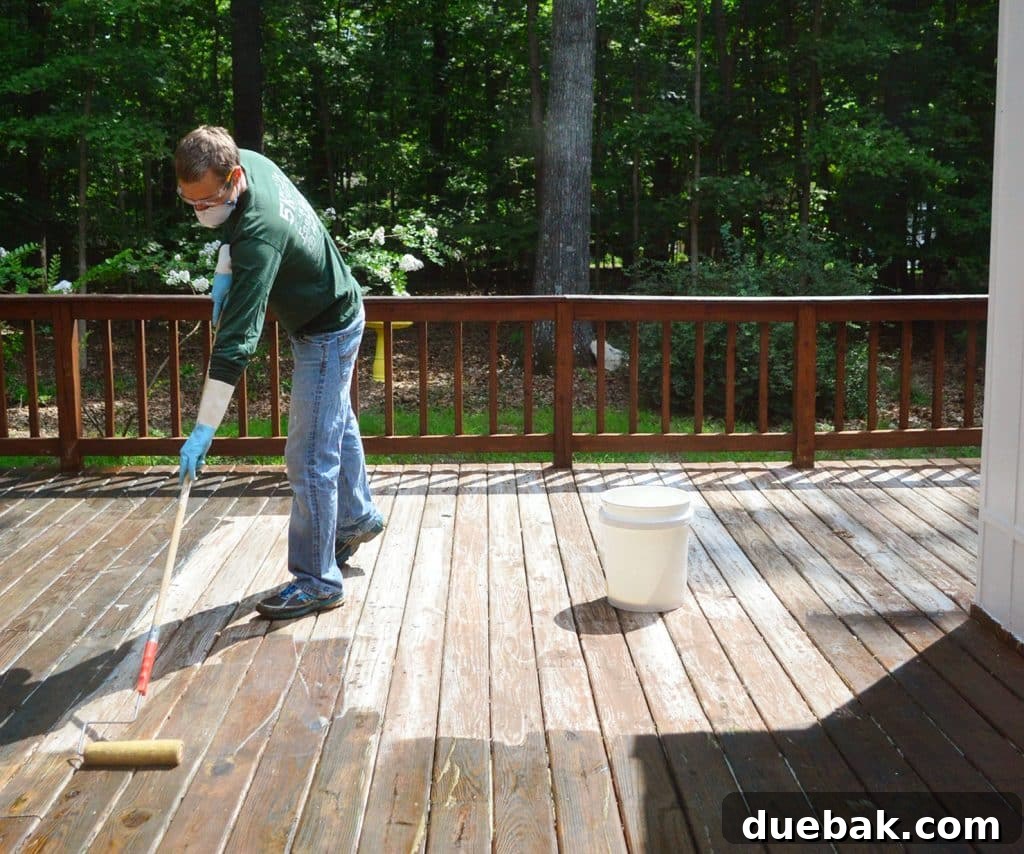 Person applying deck stripper to a wood deck under sunlight, with some areas starting to dry