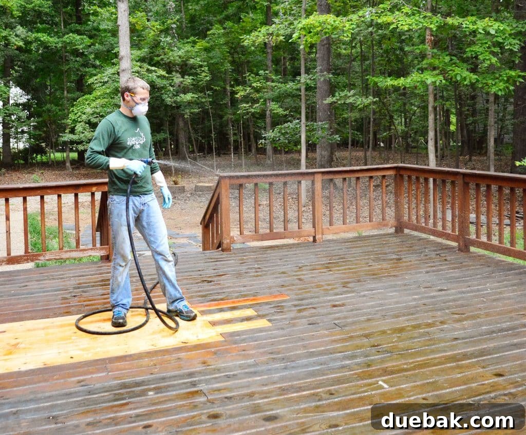 A person misting a wood deck with water to keep the chemical stripper wet and active