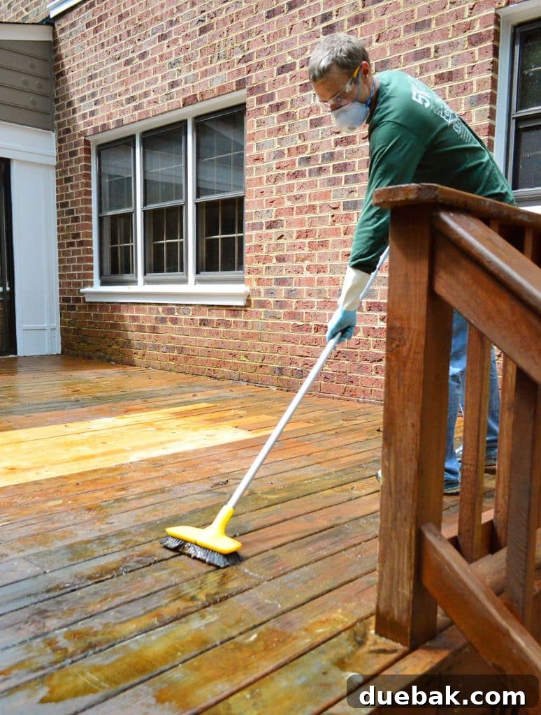 A person scrubbing a wood deck to remove old finish with a stiff brush and extension pole