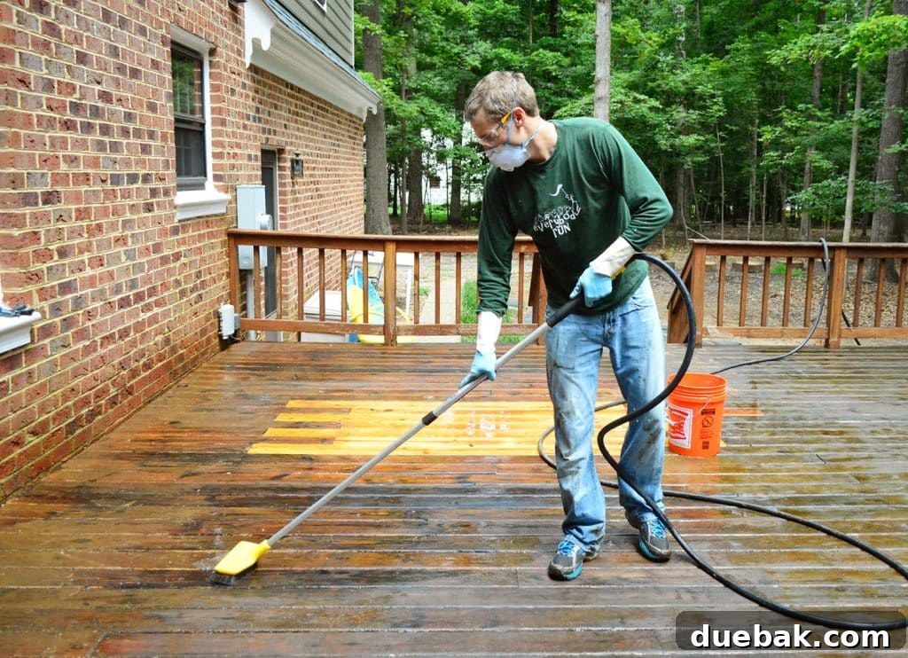 A person scrubbing a wood deck with a stiff brush that has a hose attached, allowing for simultaneous scrubbing and rinsing
