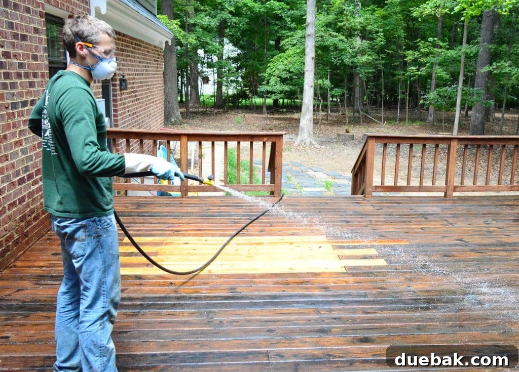 A person rinsing stripper and loosened finish off of a wood deck with a garden hose, creating clean streaks