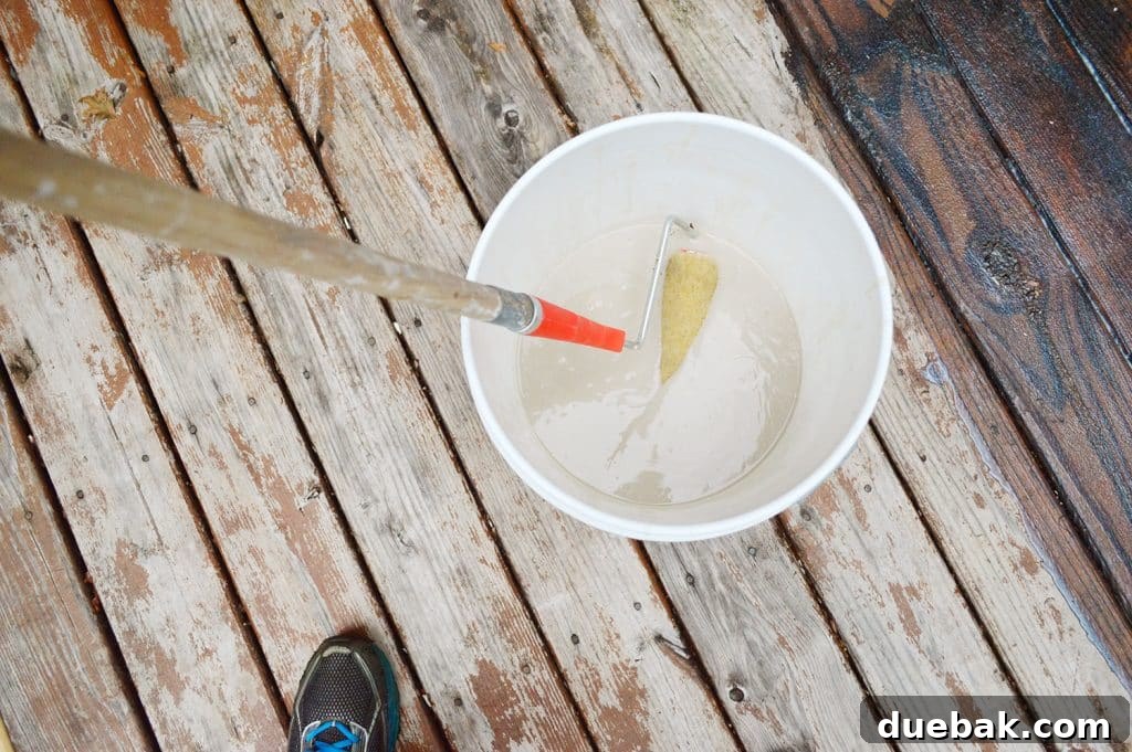 Close-up of a paint roller being dipped into a bucket of deck stain stripper, showing the thick consistency