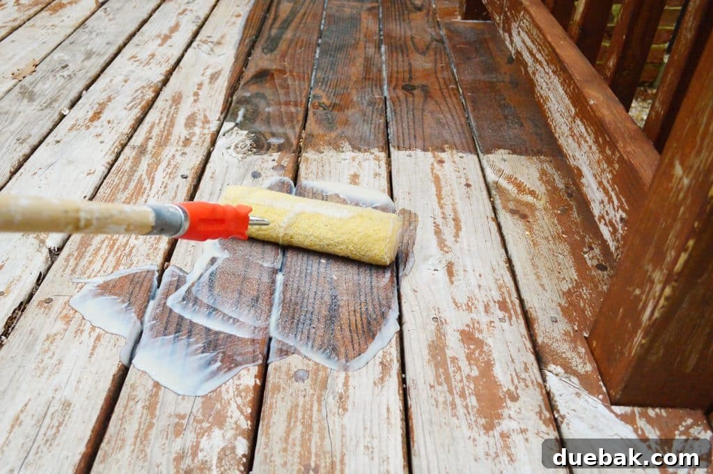 Someone rolling deck finish stripper onto a wooden deck surface, methodically covering each board