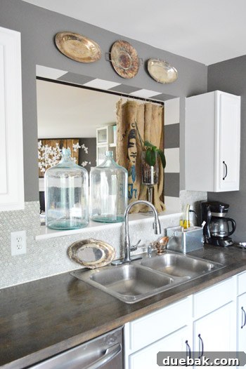 Townhouse Takeover: Unleashing Cozy Creativity 12 Kitchen view featuring burlap grain sack curtains, gleaming oversized glass containers, and gray penny tile backsplash.