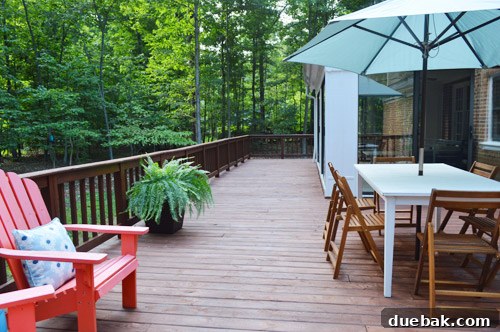 Wide shot of a newly stained deck with some furniture, showing an empty section that still needs furnishing.