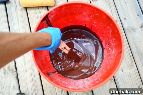 Close-up of a hand stirring the deep Russet colored deck stain in a large bucket, ensuring even color.